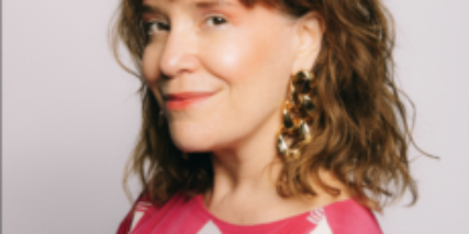 Portrait of writer Michelle Tea in a red shirt looking sideways at the camera.